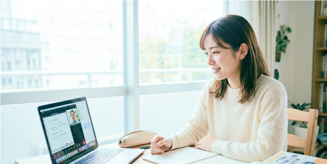 窓辺でパソコンに向かいノートを取る女性